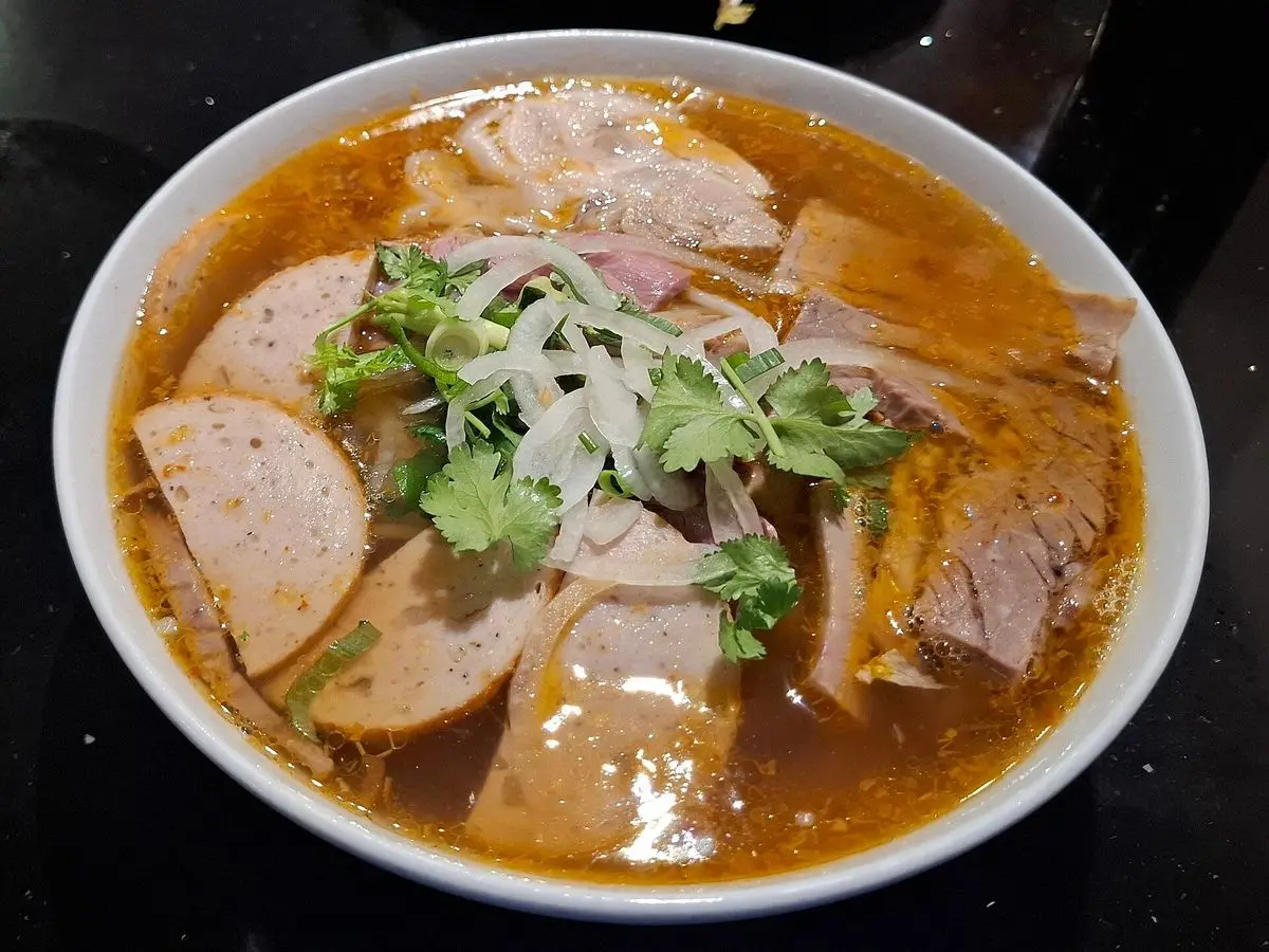 Cuenco de sopa picante de fideos de arroz con carne de ternera, embutido y hierbas frescas