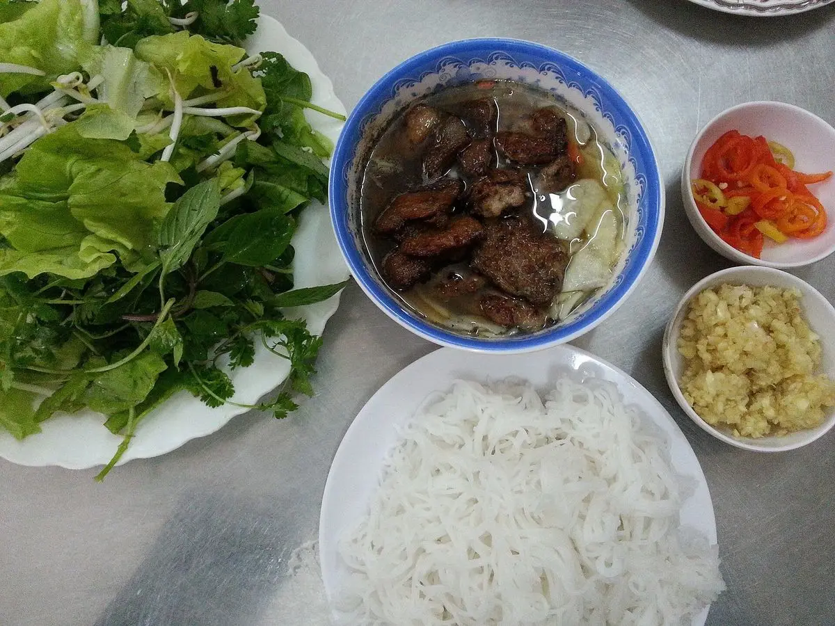 Hamburguesitas de cerdo a la parrilla en caldo con fideos de arroz, hierbas frescas y verduras