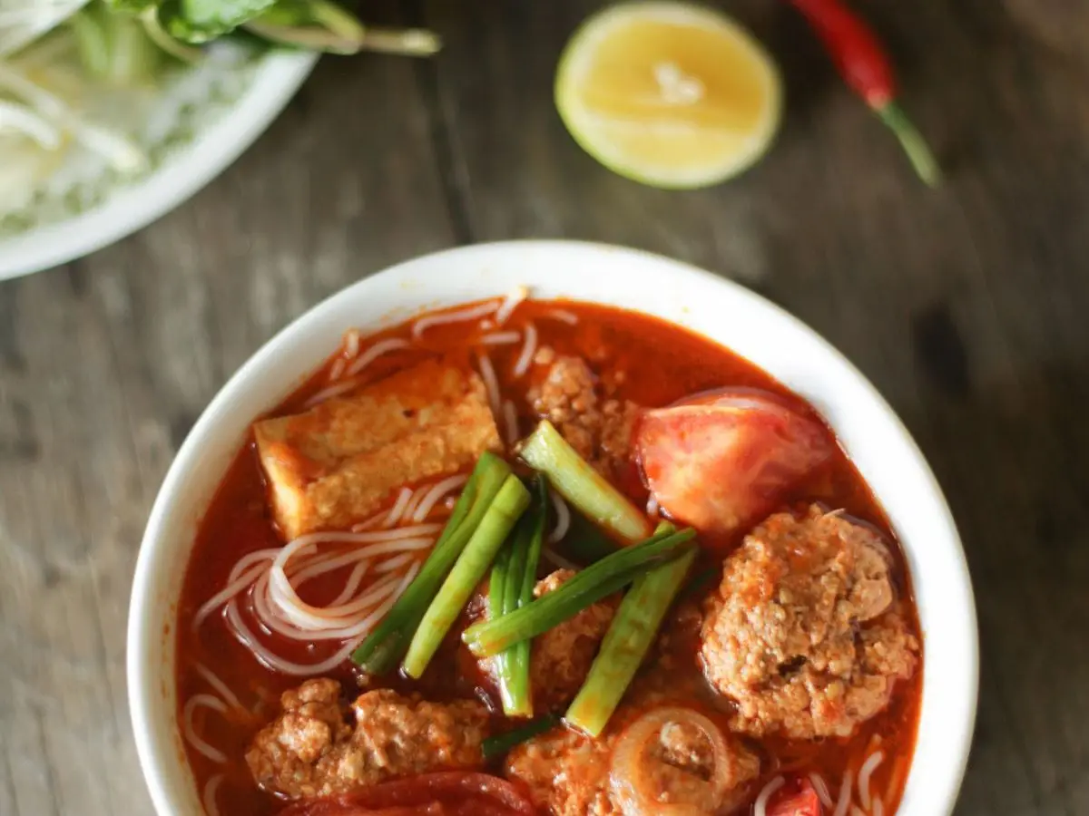 Cuenco de sopa roja de tomate con fideos de arroz, tofu frito, bolas de cangrejo y cebolleta
