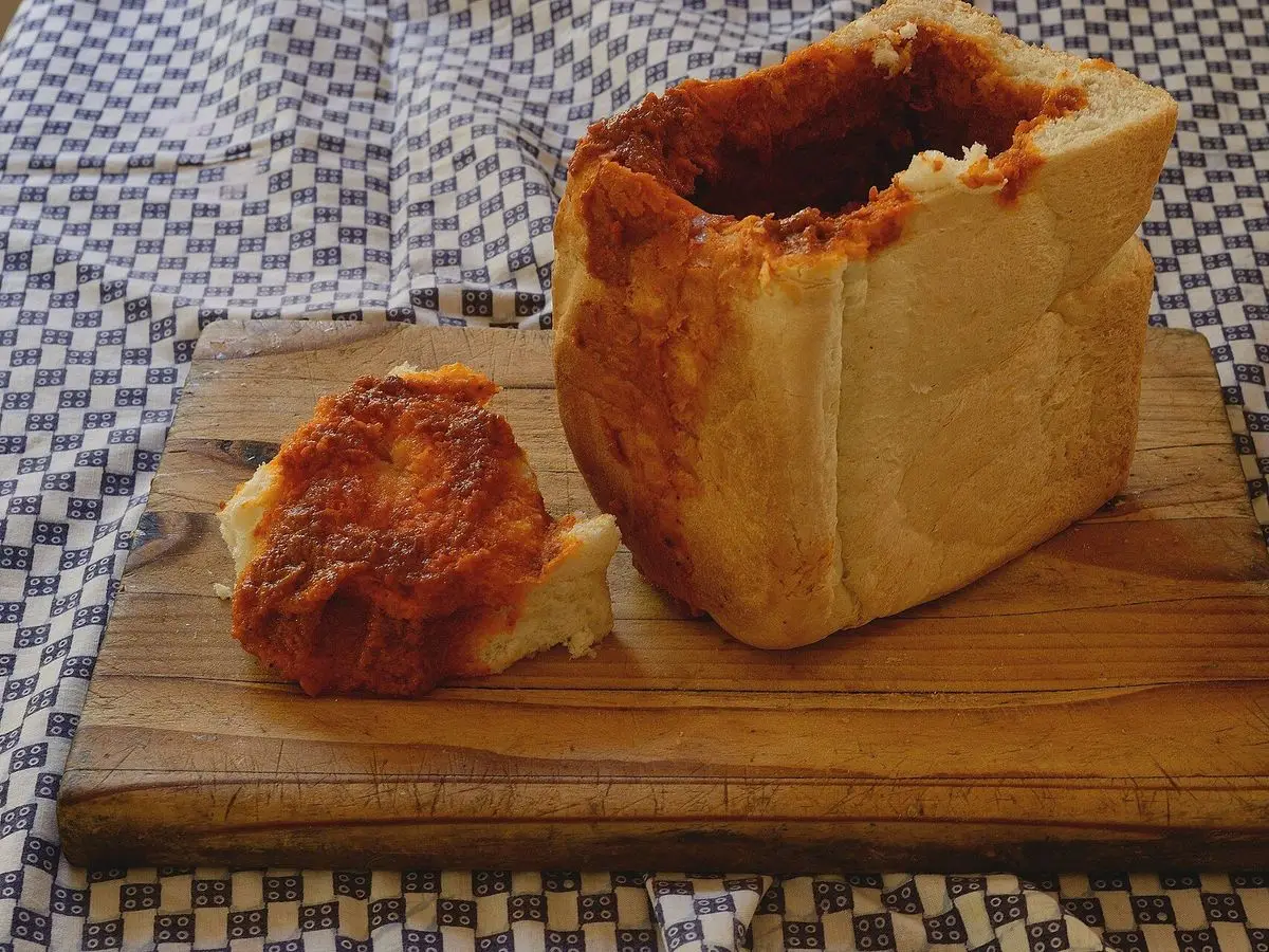 Pan de molde vaciado y relleno de curry sobre una tabla de madera, con la tapa de pan al lado