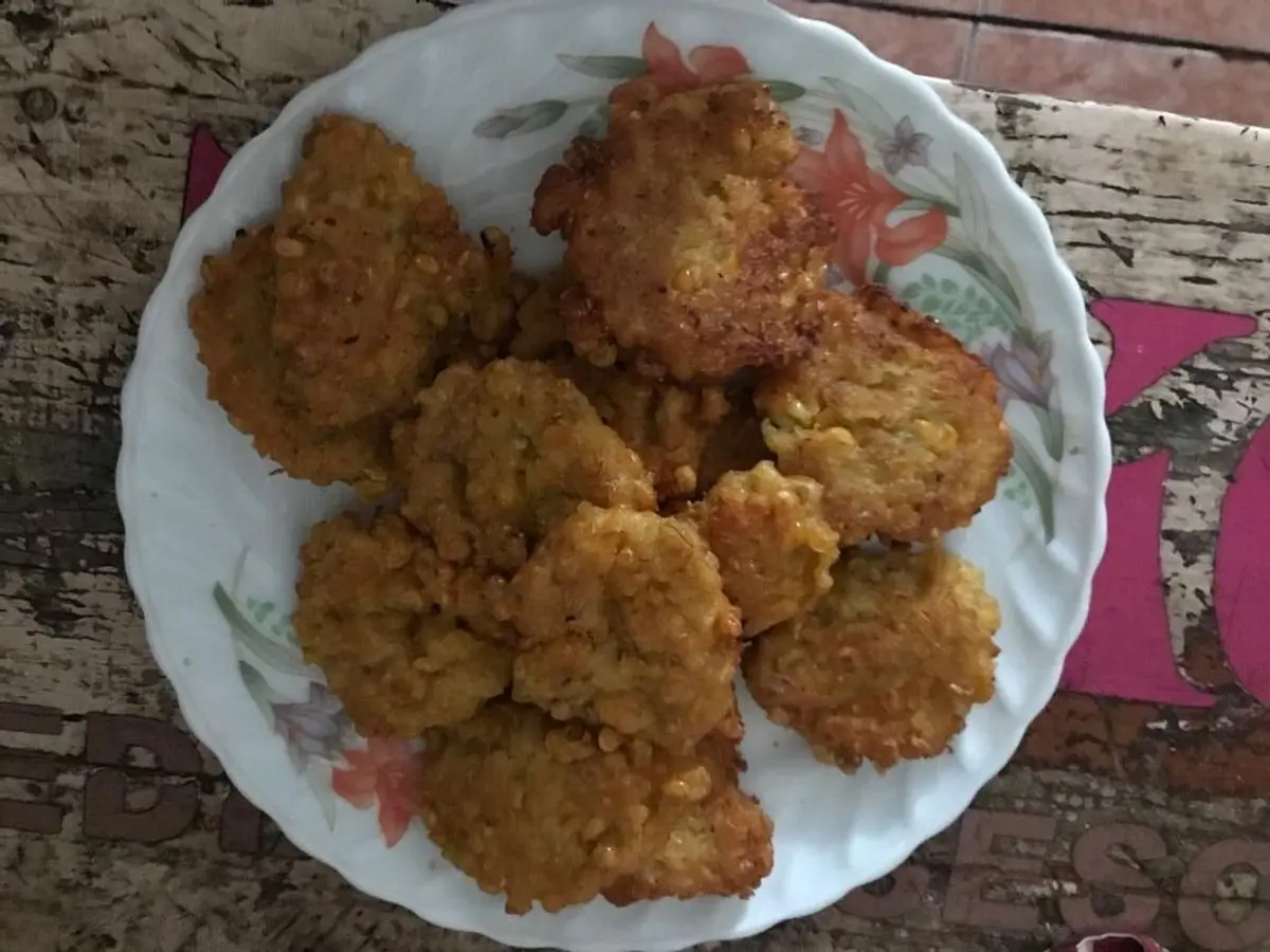 Plato de buñuelos de maíz dorados y crujientes con borde decorado sobre una mesa de madera