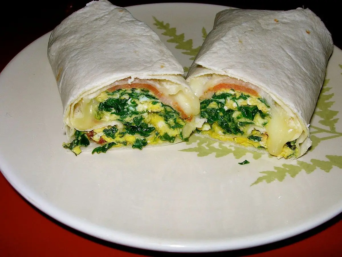Burrito de desayuno cortado por la mitad con huevo revuelto, espinacas y tomate en un plato