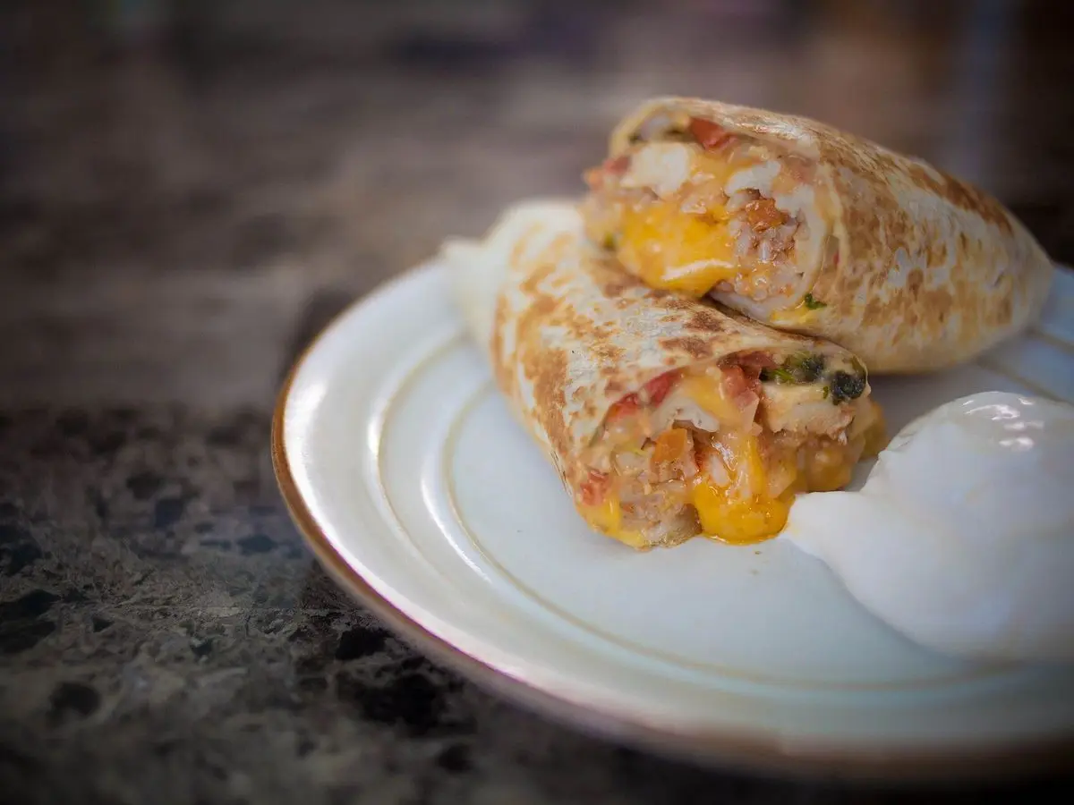 Burrito de pollo asado cortado por la mitad con queso fundido sobre un plato blanco
