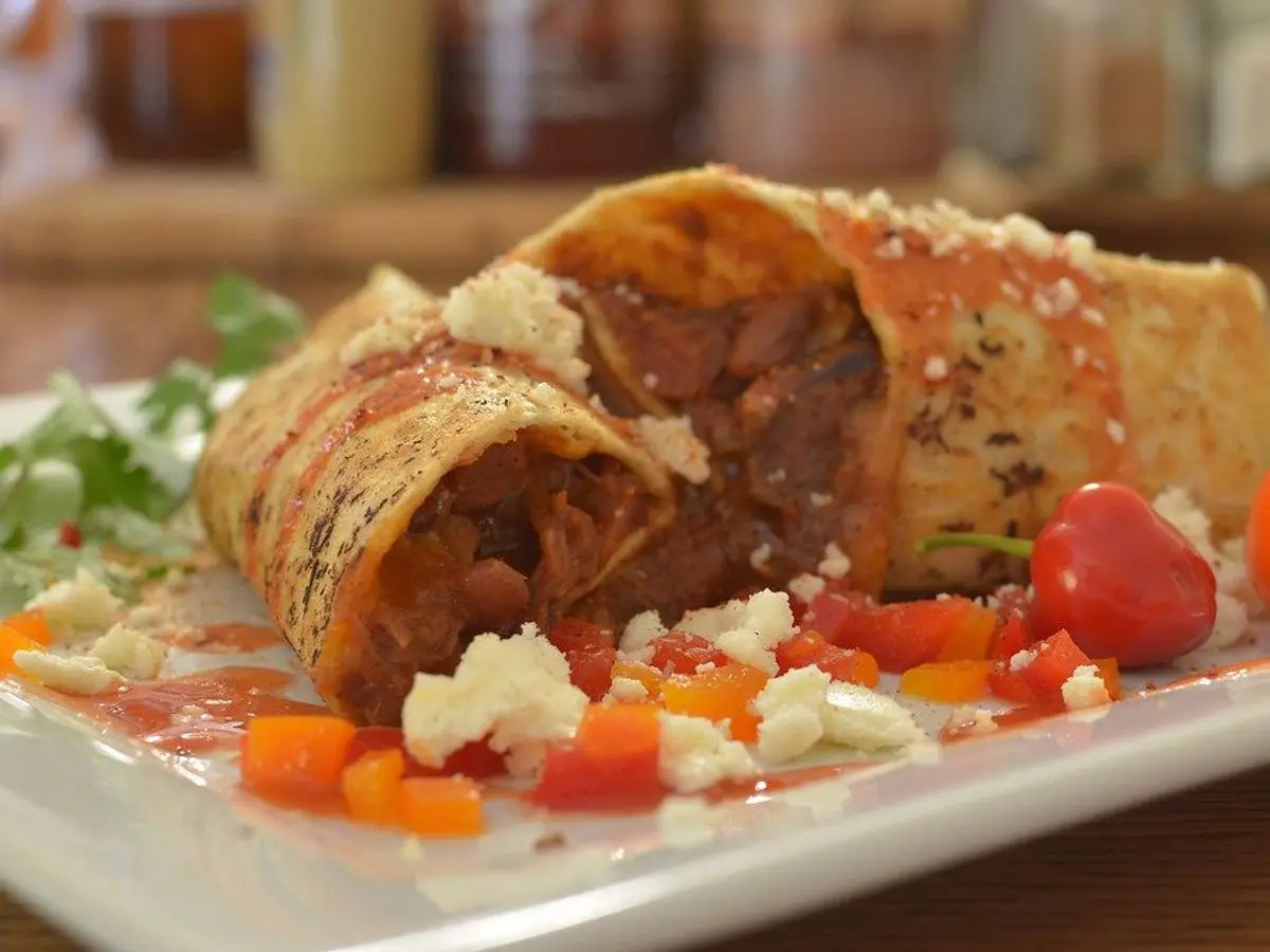 Burrito de frijoles cortado por la mitad sobre un plato con tomate y zanahoria