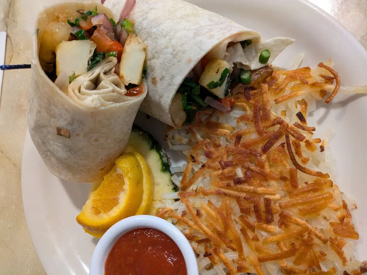 Burrito vegano cortado por la mitad relleno de tofu y verduras, con patata rallada dorada y una naranja
