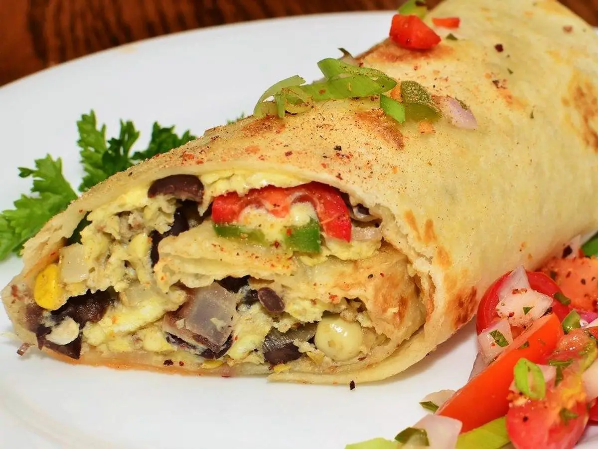 Burrito relleno de huevo revuelto con champiñones y pimiento rojo junto a ensalada de tomate