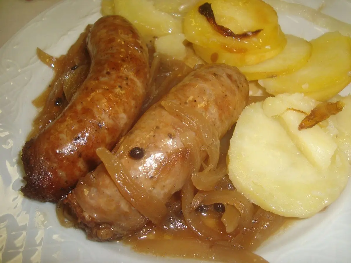 Butifarras doradas con cebolla y puré de patata en un plato blanco