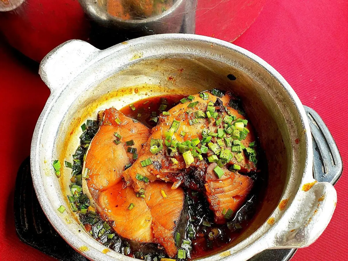 Cazuela de barro con trozos de pescado caramelizados en salsa oscura y cebolleta picada