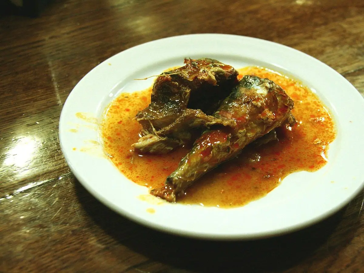 Plato blanco con pescado en escabeche cubierto de salsa anaranjada sobre una mesa de madera