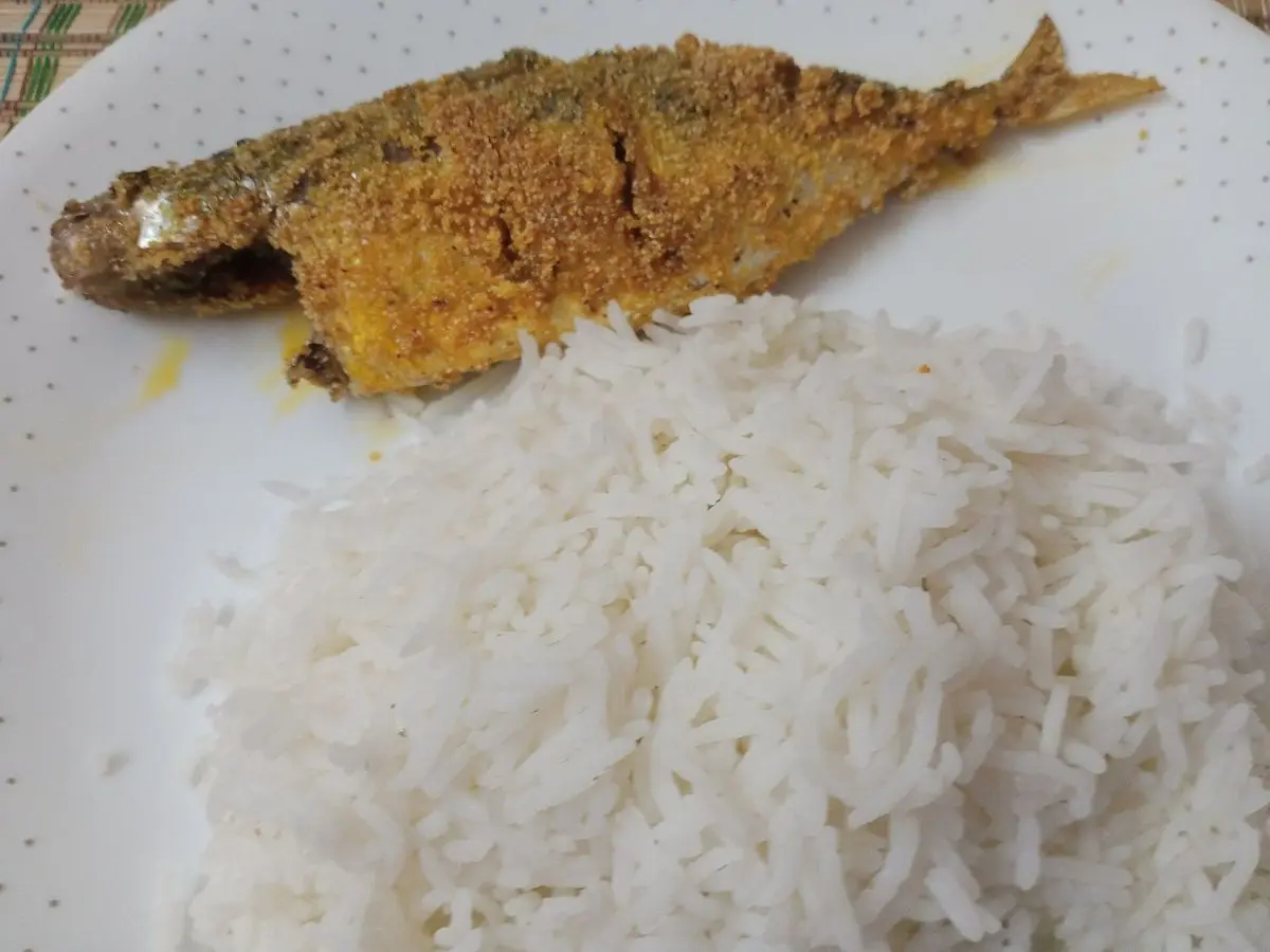 Caballa entera frita con especias junto a una porción de arroz blanco en un plato blanco