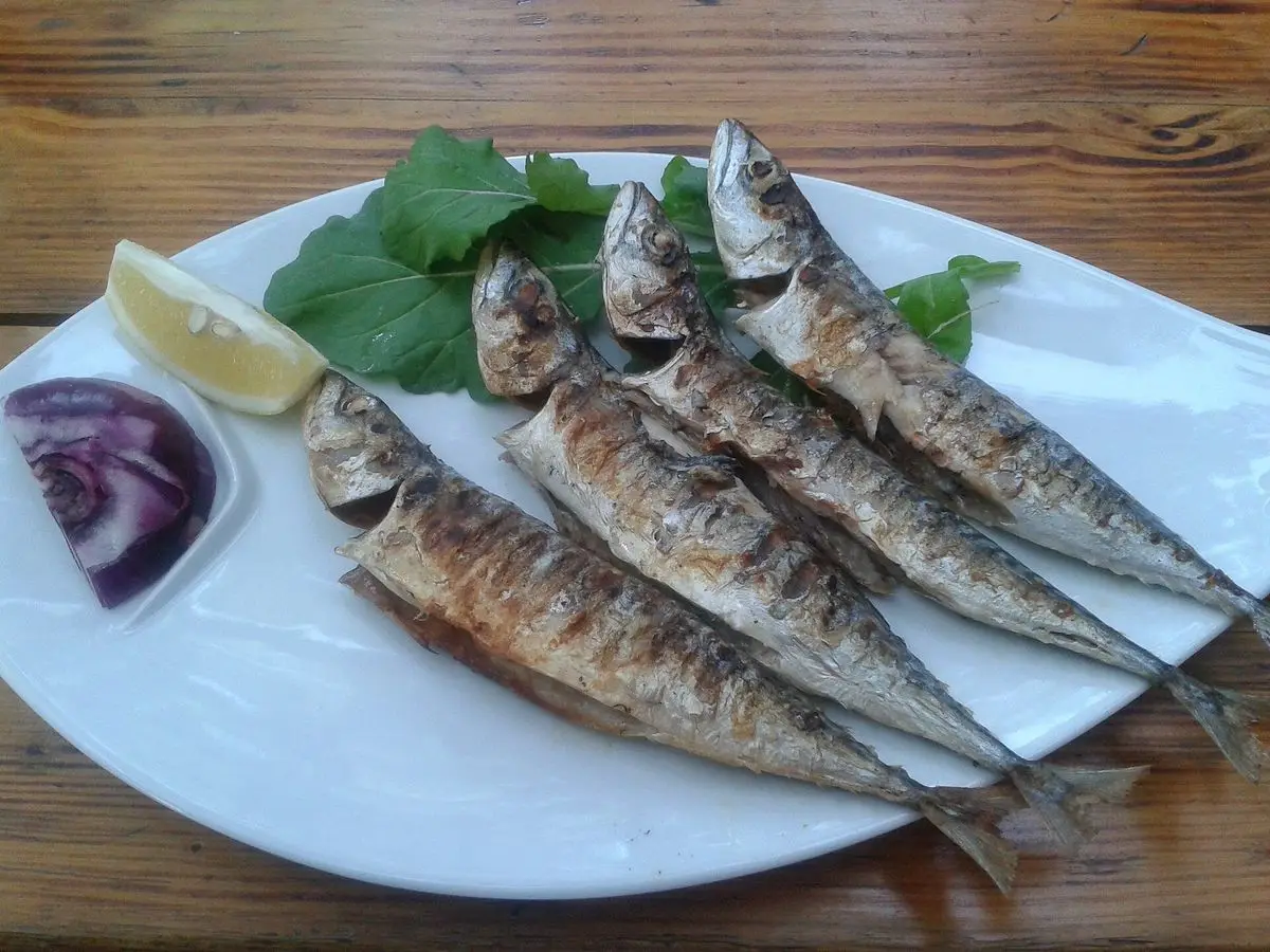 Caballas a la plancha en un plato blanco con rodaja de limón, hojas verdes y cebolla morada