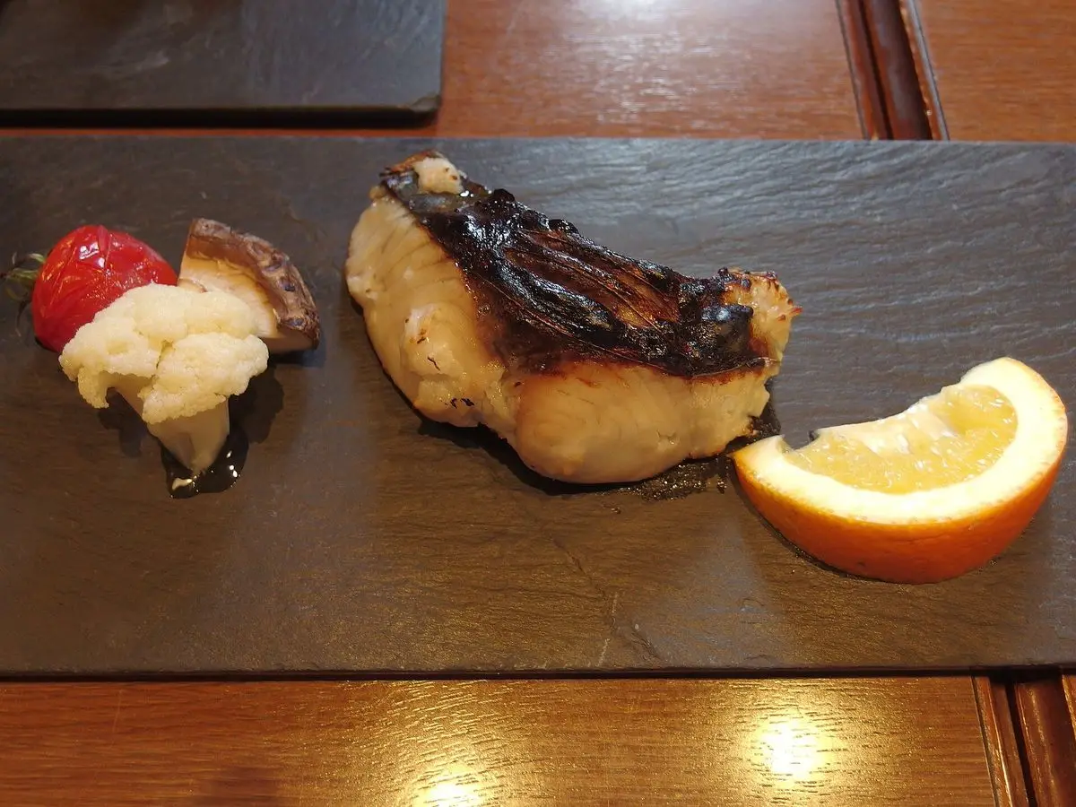 Filete de caballa a la plancha dorado sobre pizarra negra con rodaja de naranja y guarnición