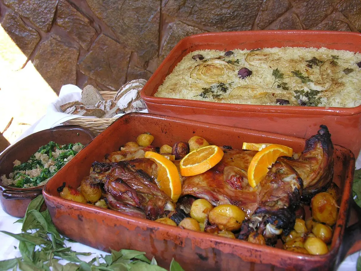 Fuente de barro con cabrito asado, patatas doradas y rodajas de naranja