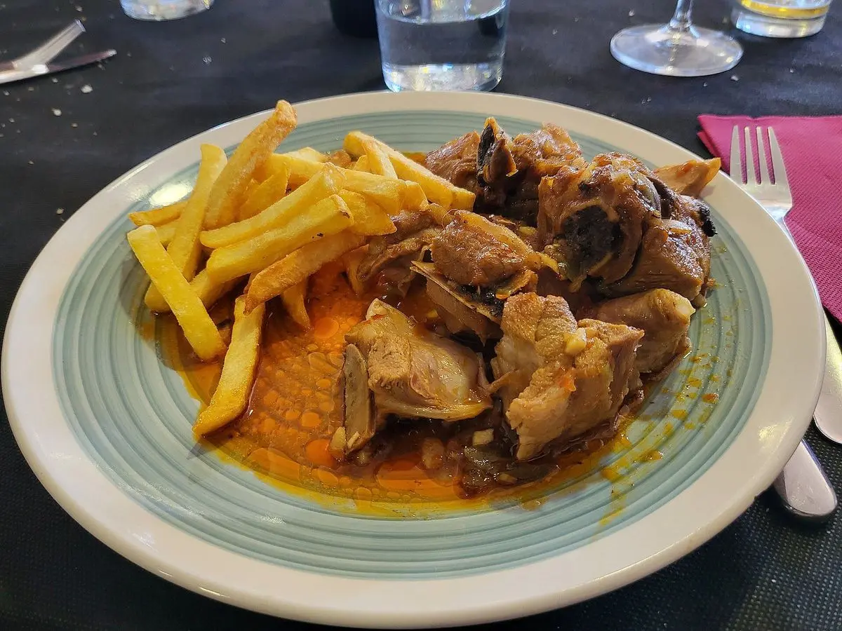 Plato de carne guisada en salsa rojiza acompañada de patatas fritas