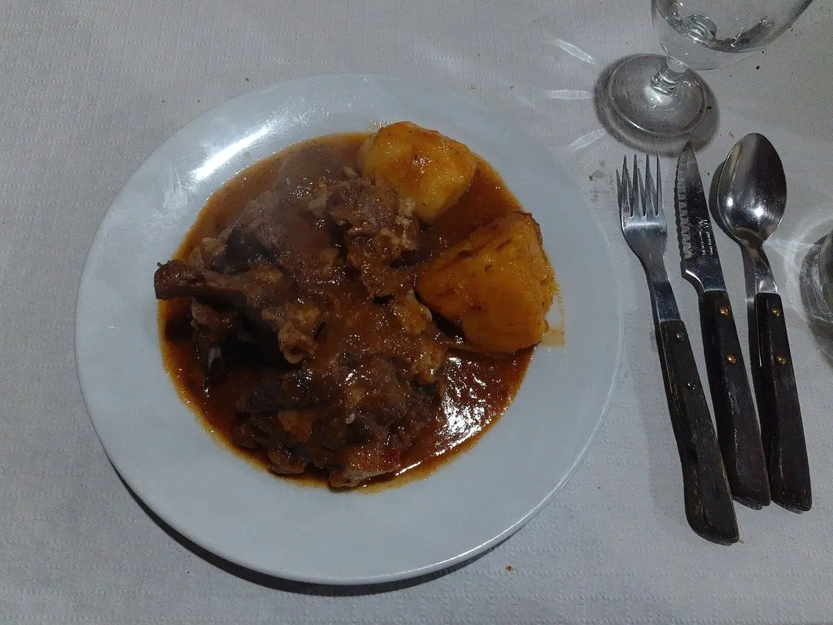 Plato blanco con cabrito guisado en salsa oscura y trozos de patata