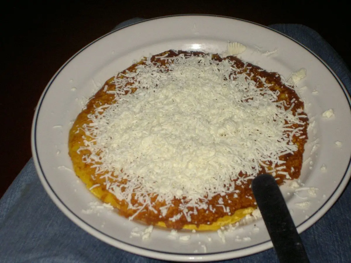 Cachapa de maíz en un plato cubierta de queso blanco rallado