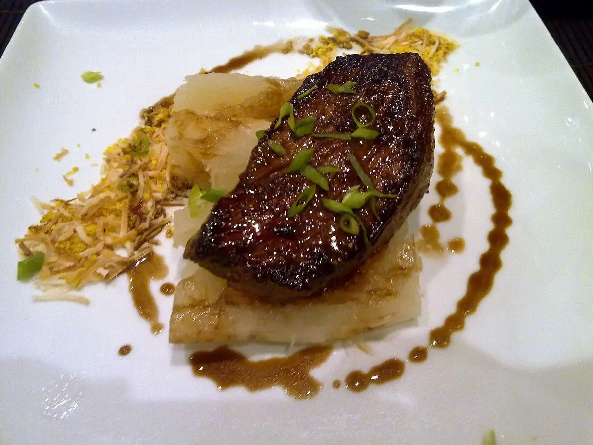 Filete de carne de vaca a la plancha sobre base clara con farofa dorada y salsa oscura en un plato cuadrado