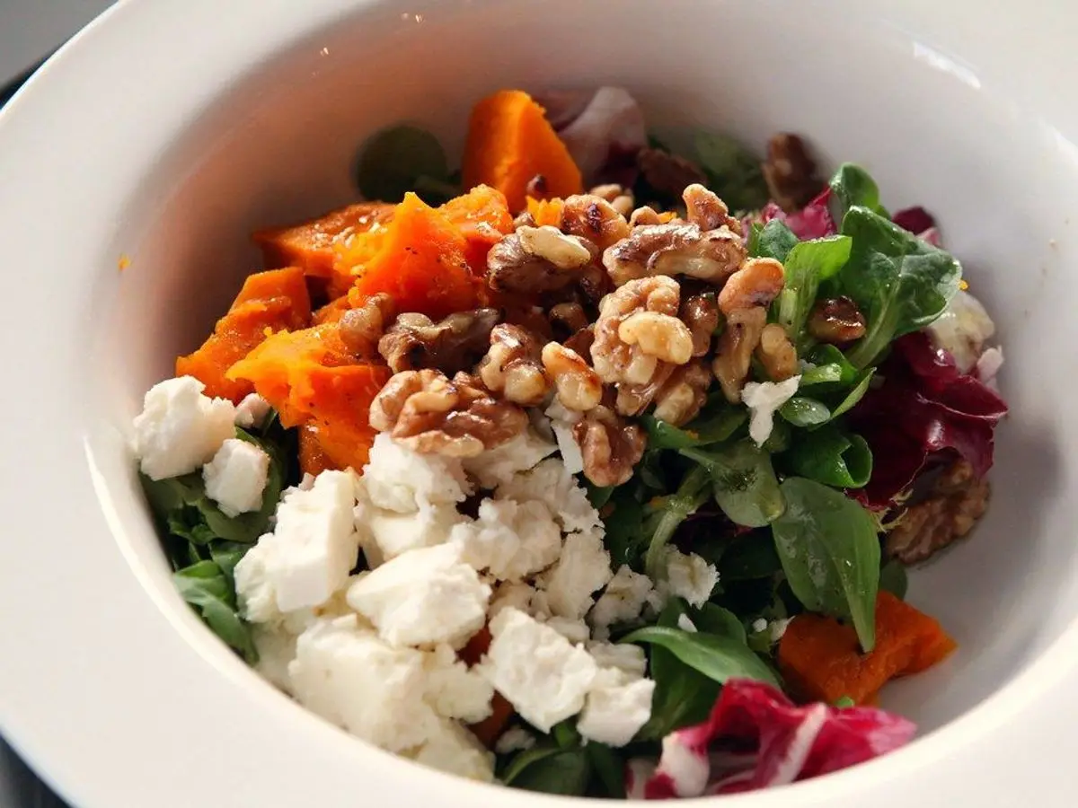 Cuenco de ensalada con calabaza asada, queso feta desmenuzado, rúcula, nueces y cebolla morada