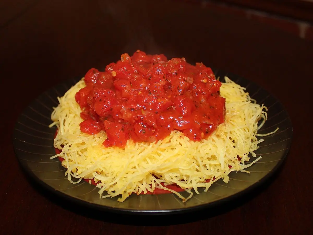 Hebras de calabaza espagueti cocida con salsa de tomate roja por encima en un plato oscuro