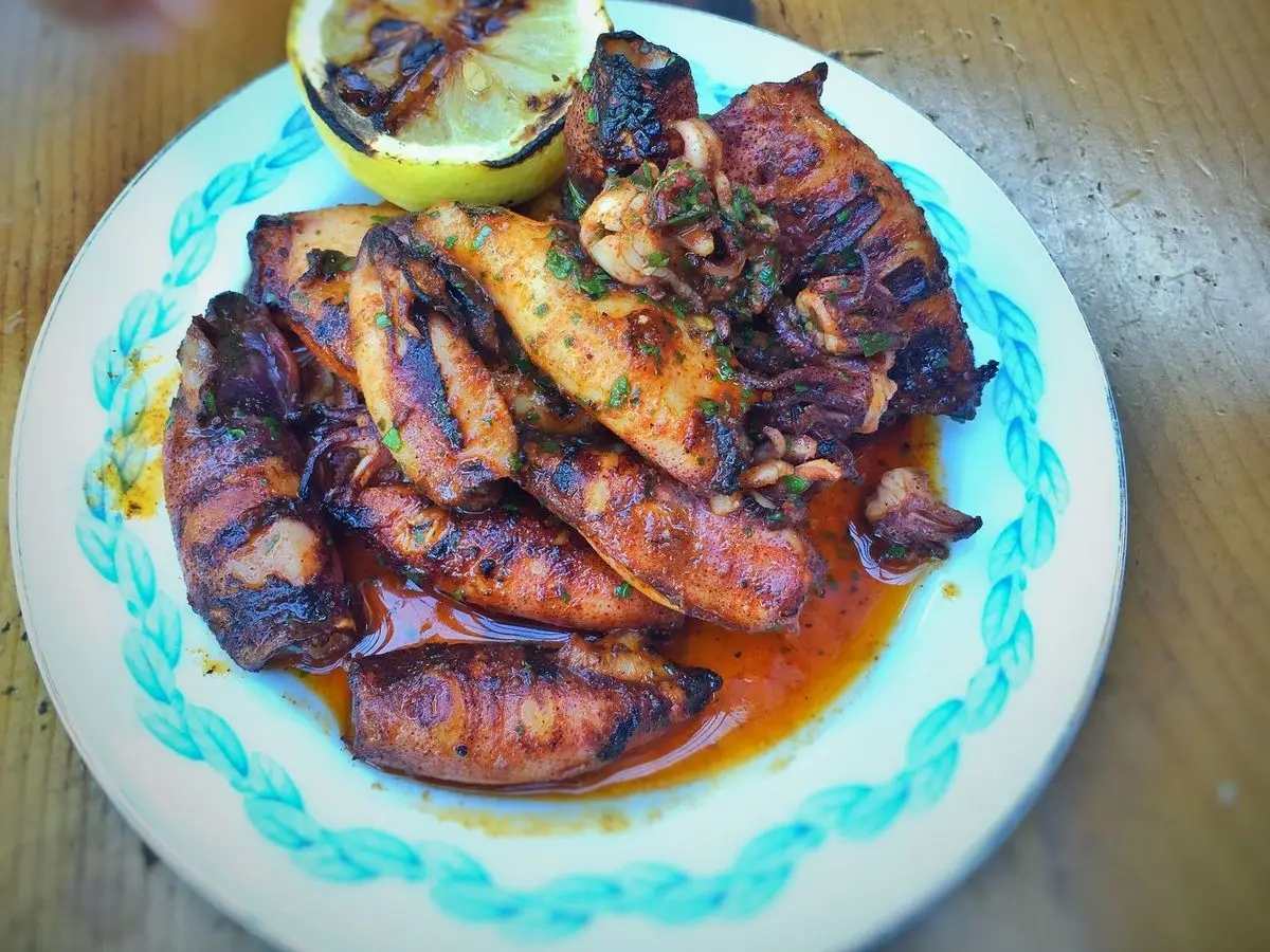 Calamares a la plancha con pimentón y perejil picado, con medio limón asado, en un plato de borde azul