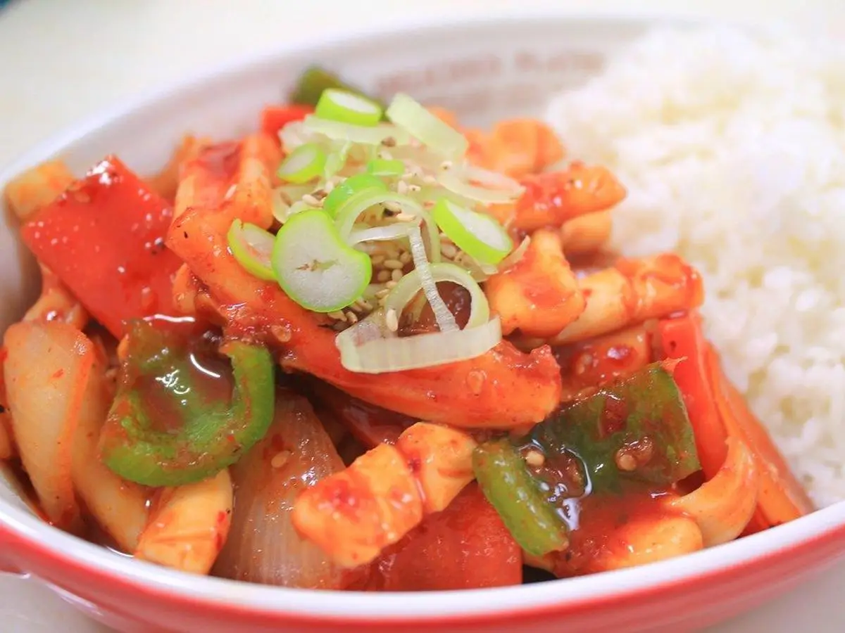 Cuenco con calamar y pimiento rojo y verde en salsa, con cebolleta y arroz blanco
