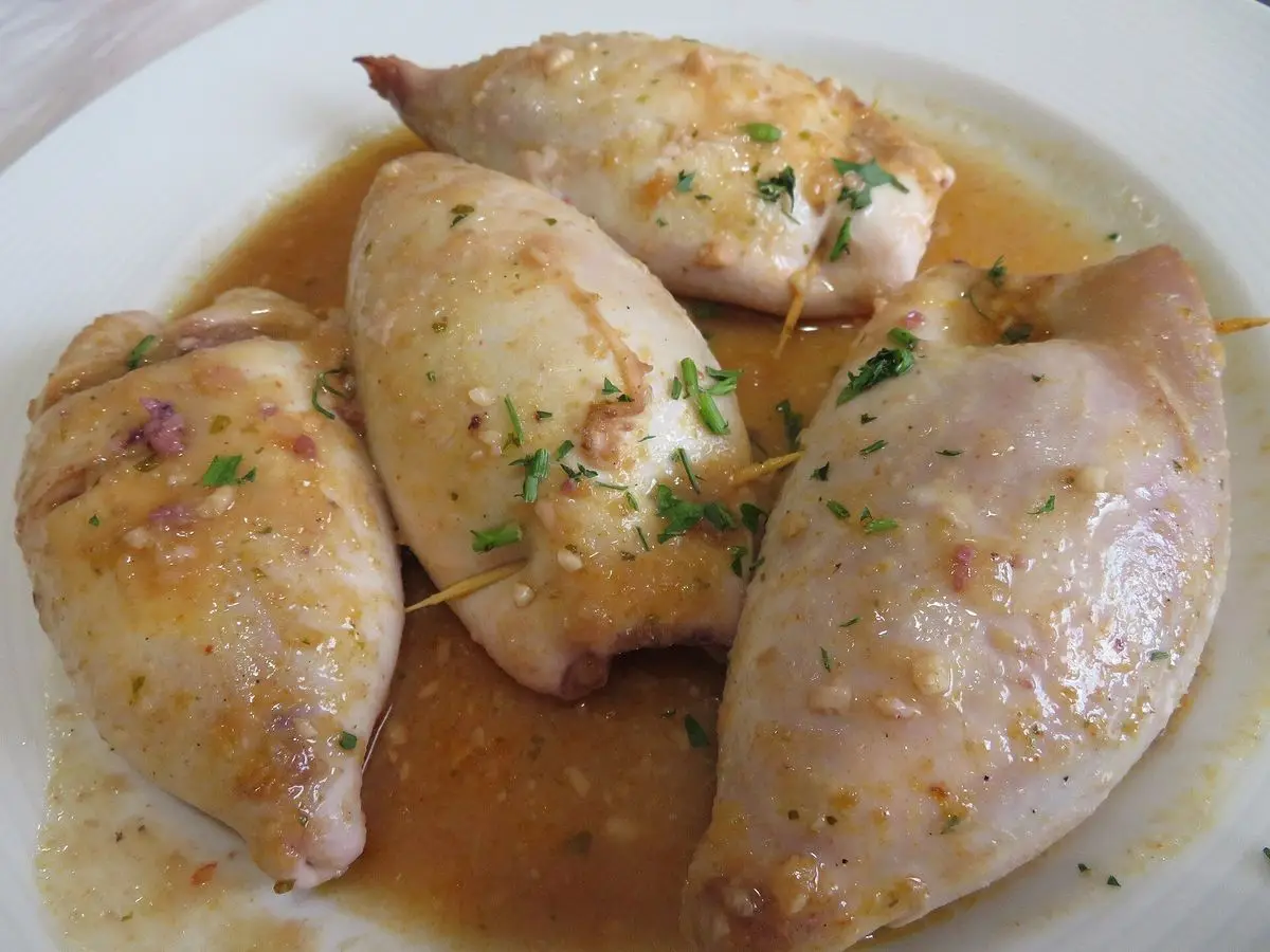 Calamares rellenos enteros en su salsa, espolvoreados con perejil picado en un plato blanco
