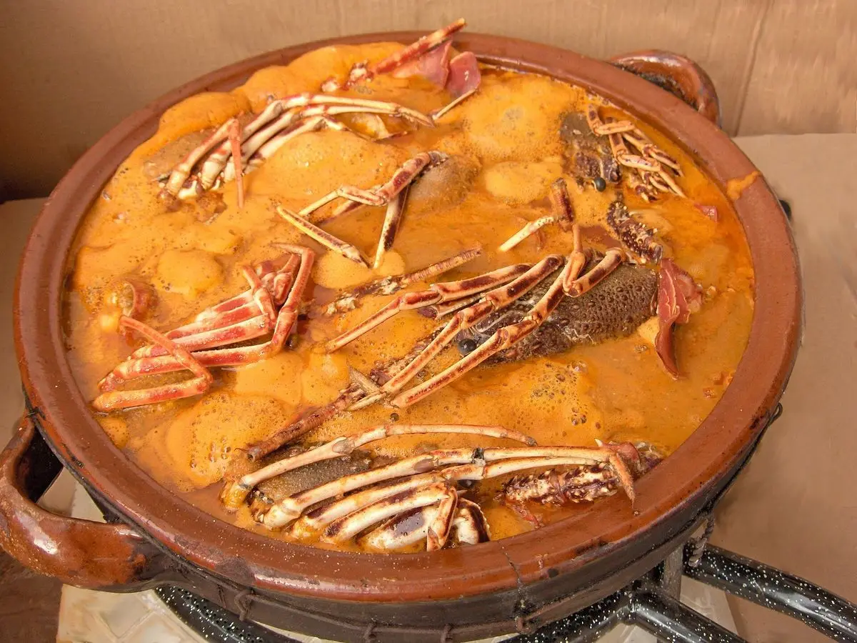 Cazuela de barro con caldereta de langosta, salsa anaranjada y patas de crustáceo por encima