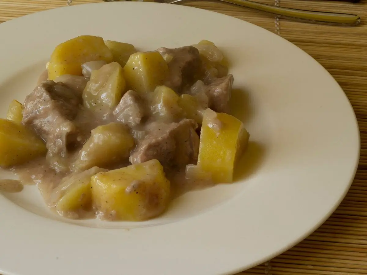 Plato llano con trozos de ternera guisada y dados de patata en salsa clara