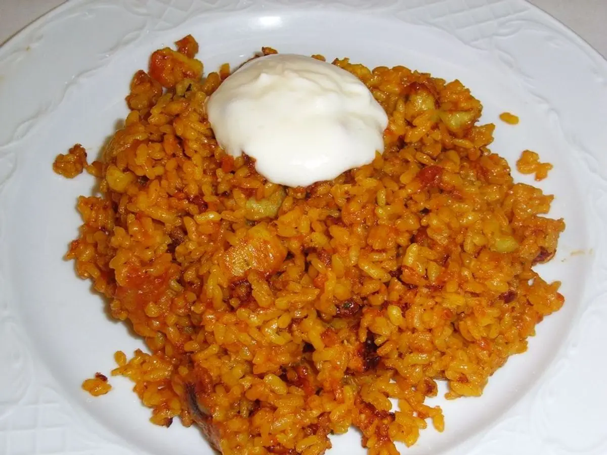 Plato blanco de arroz a banda anaranjado con una cucharada de alioli encima
