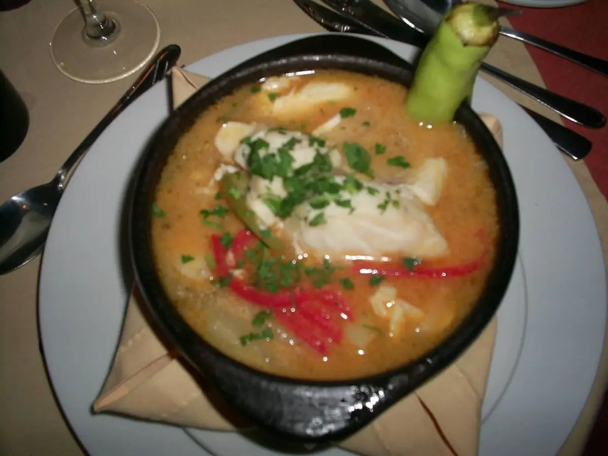 Cazuela negra de caldillo de congrio con patata, pimiento rojo y cilantro sobre un plato blanco