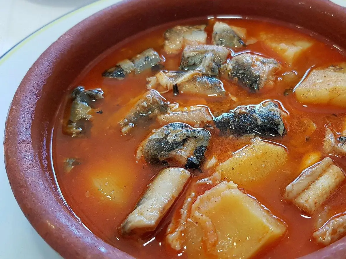 Cazuela de barro con trozos de pescado y patatas en un caldo rojo de pimentón