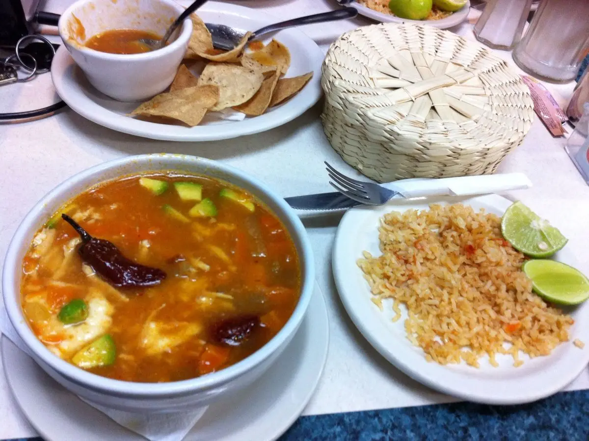 Cuenco de caldo tlalpeño con pollo, aguacate y chile seco, con arroz rojo y tostadas al lado