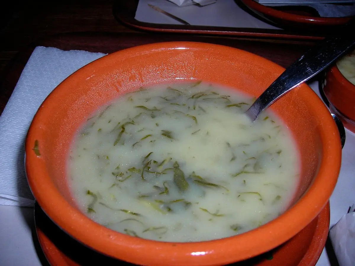 Cuenco de barro anaranjado con caldo verde cremoso de patata y col en tiras finas