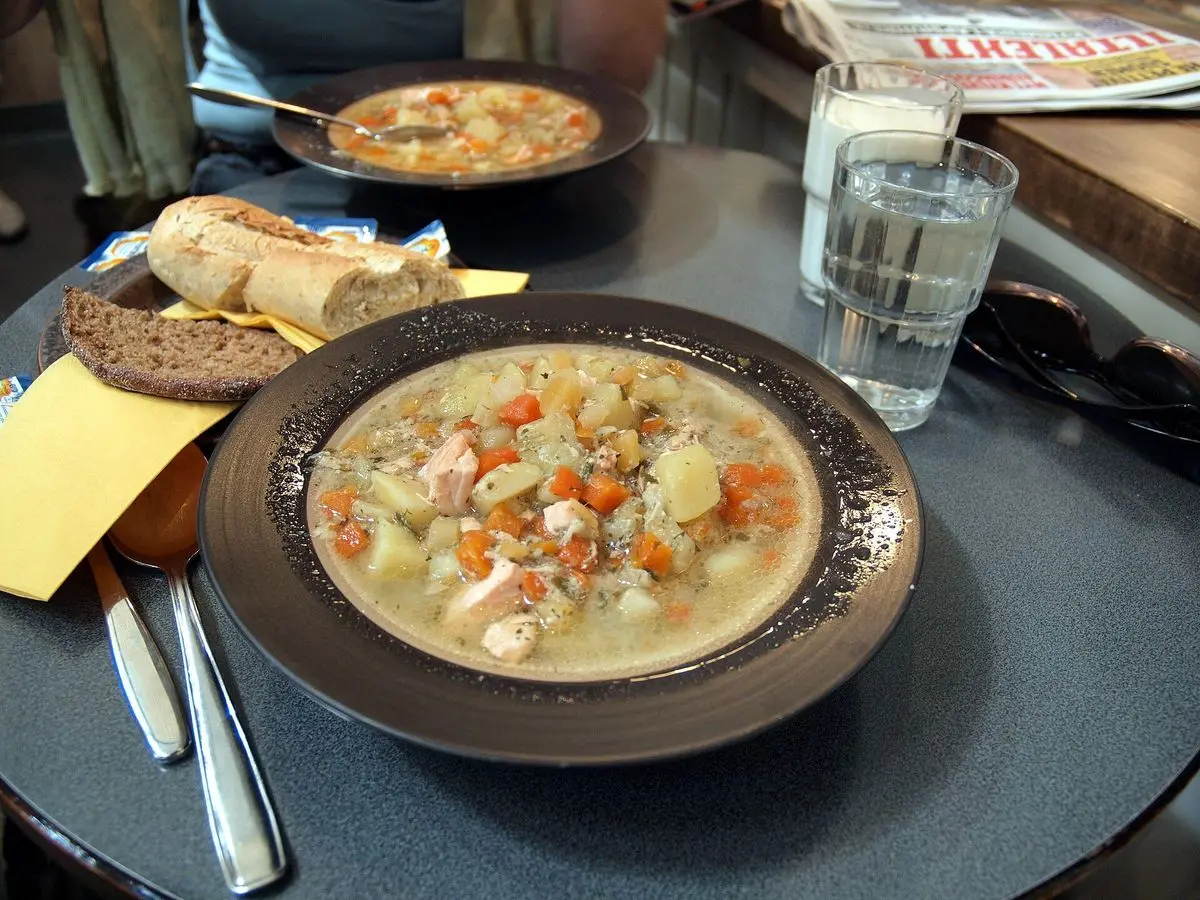 Plato hondo de sopa de pescado con zanahoria y trozos de pescado, junto a pan de centeno