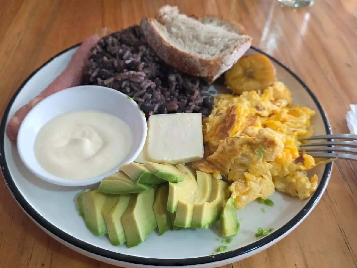 Plato de desayuno latinoamericano con arroz y alubias, huevo revuelto, aguacate, queso y pan