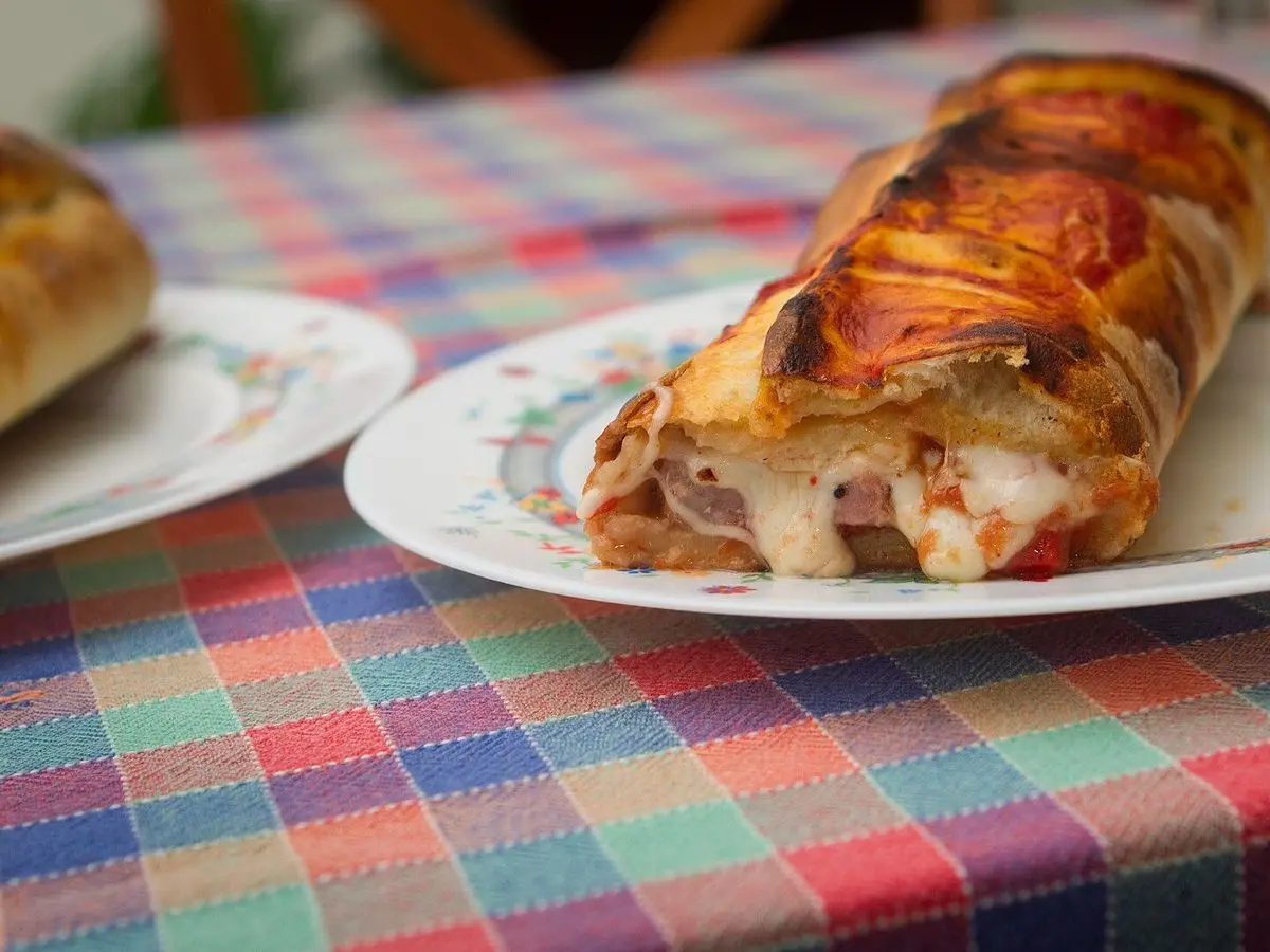 Calzone dorado relleno con queso y tomate servido en un plato sobre un mantel de cuadros