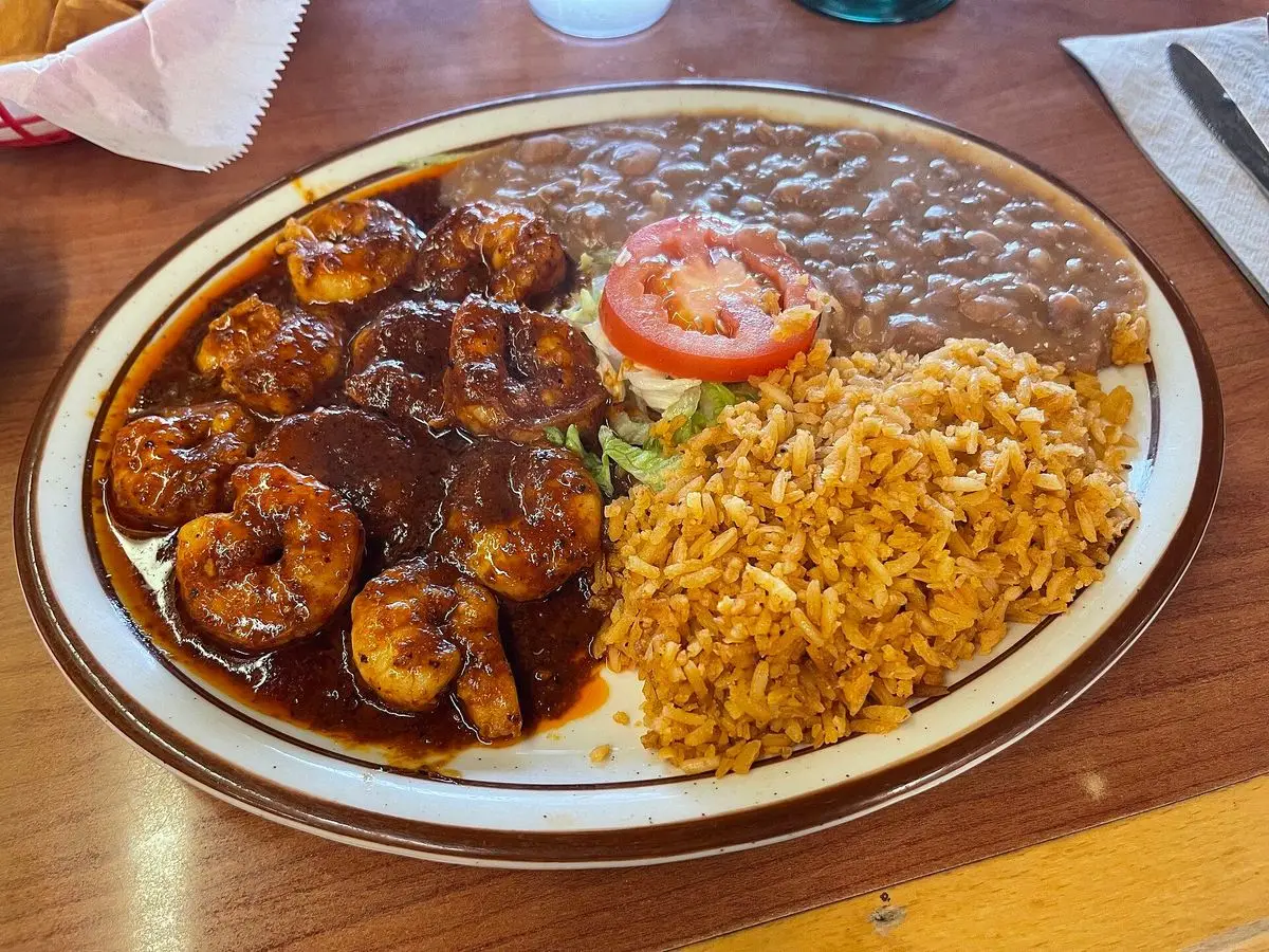 Plato con gambas en salsa roja picante, rodaja de tomate, arroz rojo y frijoles refritos