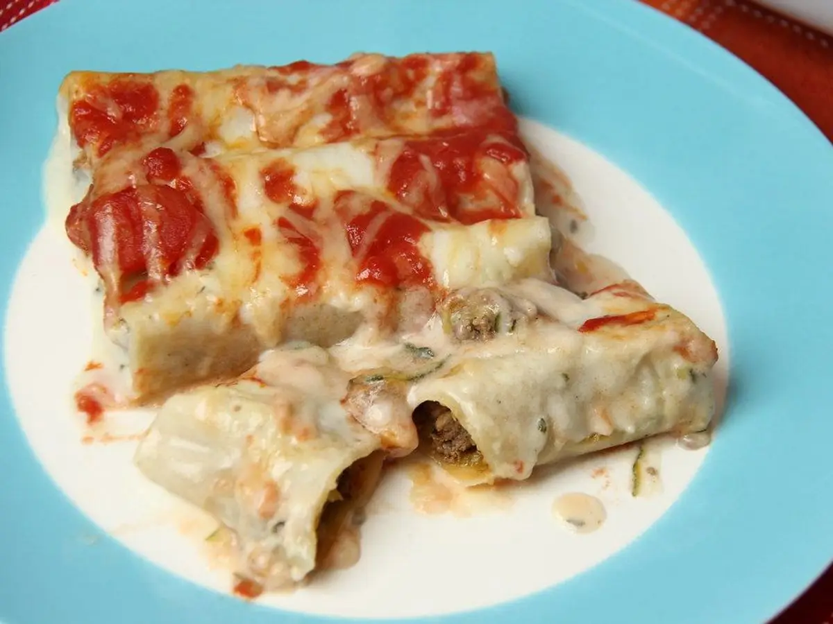 Canelones gratinados con salsa de tomate y bechamel sobre un plato turquesa