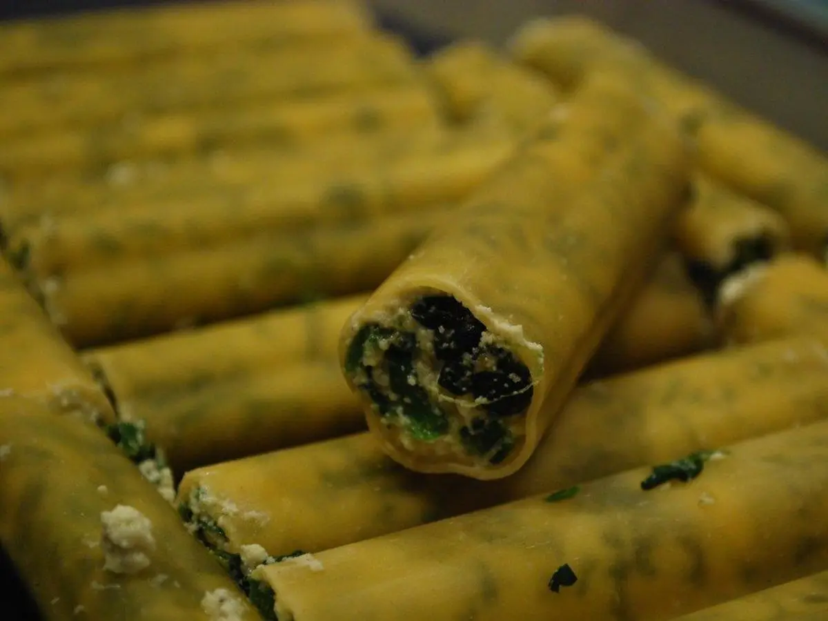 Canelones rellenos de espinacas en una fuente, uno abierto mostrando el relleno verde