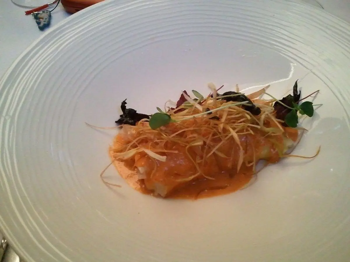 Plato blanco redondo con canelón de marisco con salsa de tomate y hierbas por encima