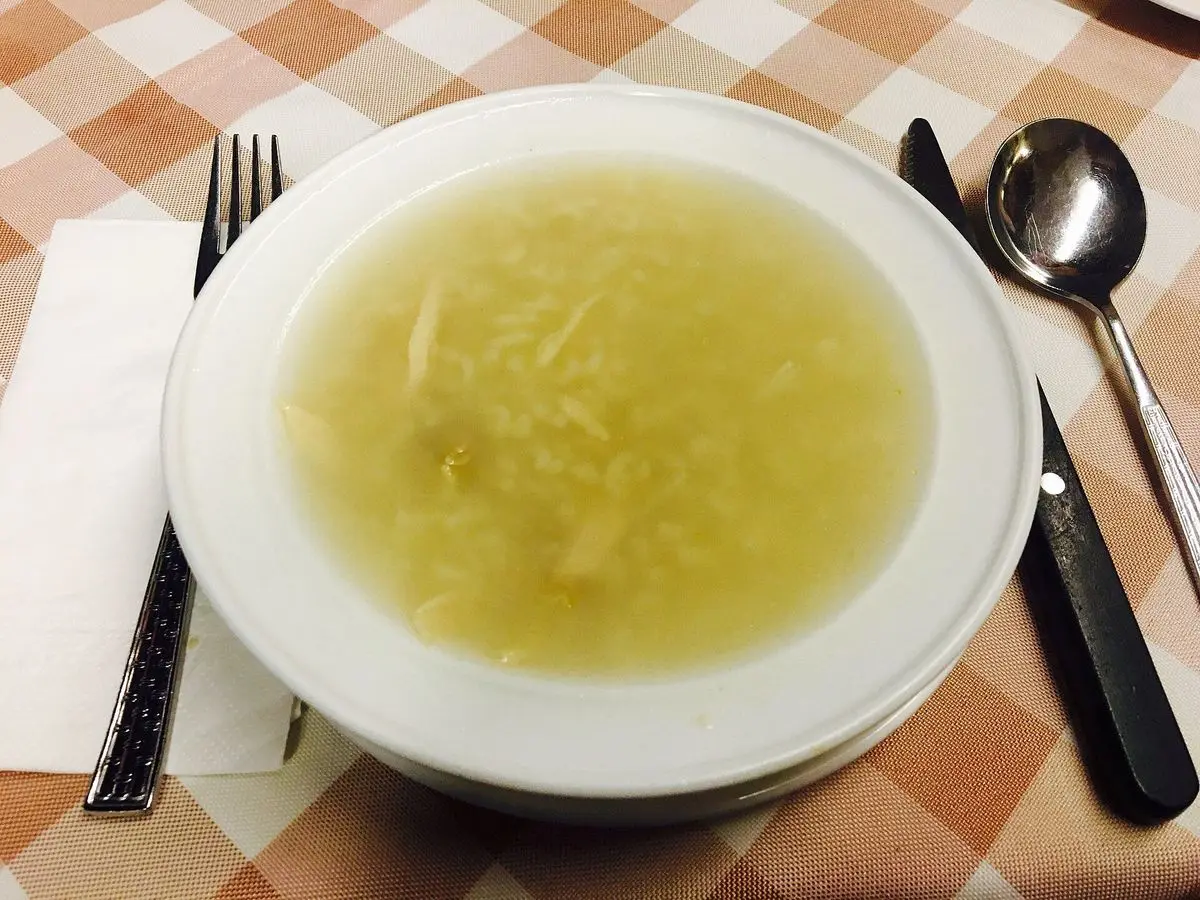 Plato hondo blanco de caldo de pollo con arroz sobre un mantel de cuadros naranjas