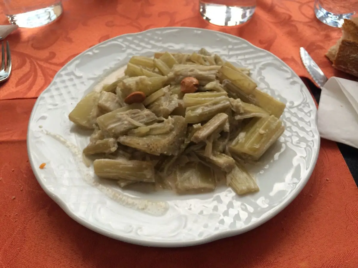 Plato de pencas de verdura guisadas en salsa clara de almendras, con almendras enteras, sobre un mantel naranja