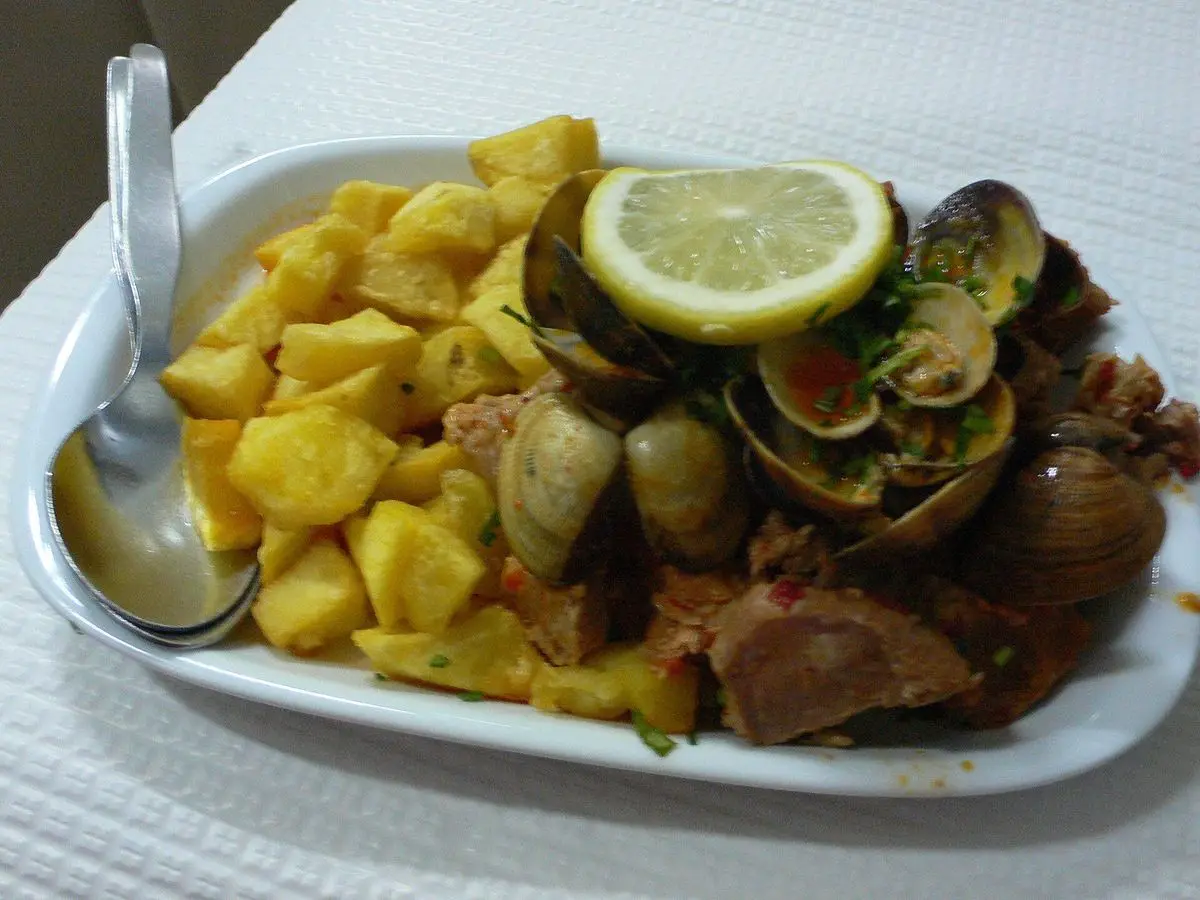 Cerdo con almejas y patatas fritas en cubos con rodaja de limón en una fuente blanca