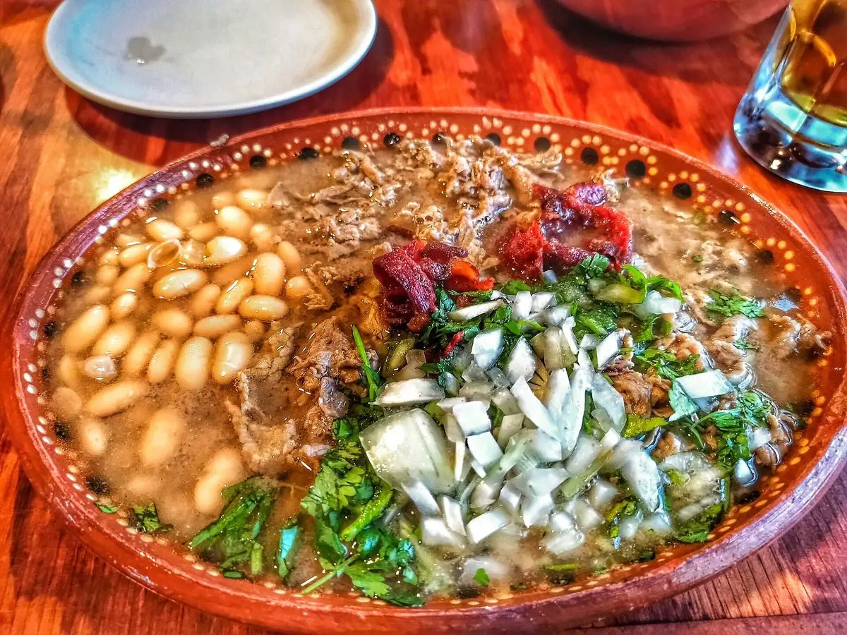 Fuente de barro con carne en su jugo, frijoles pintos, cebolla picada, cilantro y rabanitos