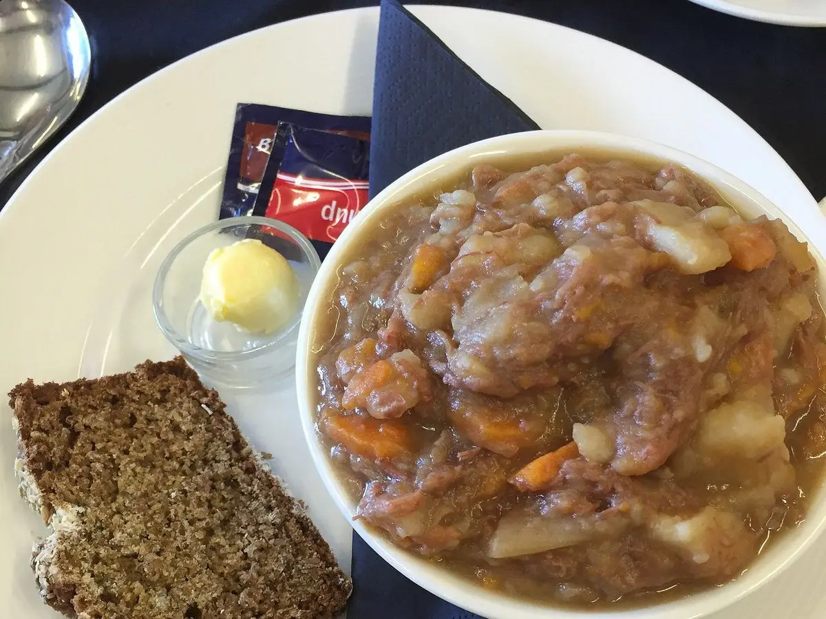 Cuenco blanco de guiso de carne con patata y zanahoria junto a una rebanada de pan