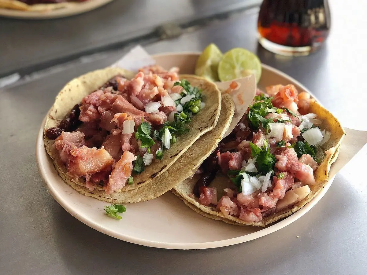 Dos tacos de carnitas de cerdo con cebolla y cilantro sobre tortillas de maíz en un plato con lima