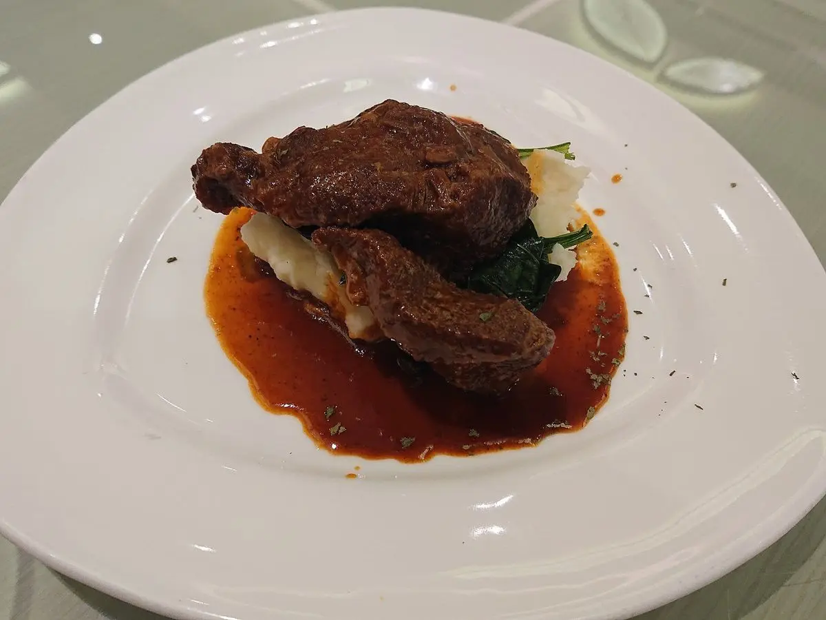 Plato blanco con carrillada de ternera guisada sobre puré de patata en salsa oscura