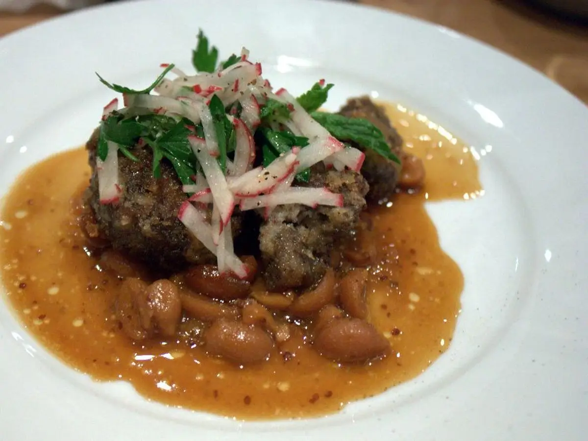 Carrilleras de cerdo estofadas en salsa sobre judías, con rabanitos y hierbas frescas