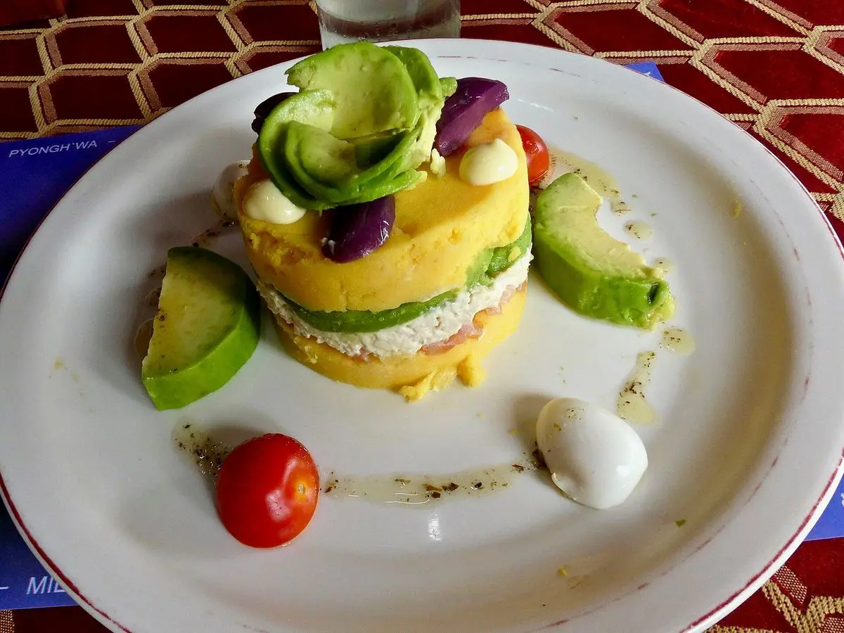 Torre de puré de patata amarilla con relleno y aguacate, huevo cocido y tomate cherry en un plato