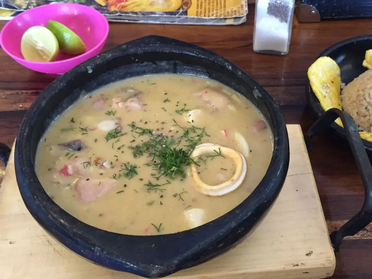Cazuela de mariscos en salsa cremosa con anillas de calamar, junto a arroz y patacones
